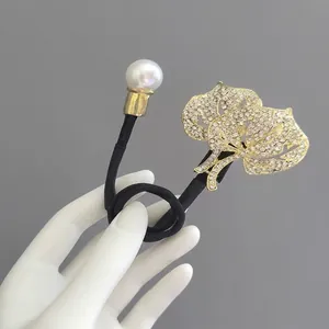 Détail d'un élastique élégant avec perle blanche et pendentifs feuilles dorées en strass