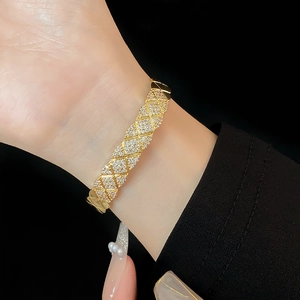Detail of gold quilted bangle with shimmering zircons worn against a black backdrop
