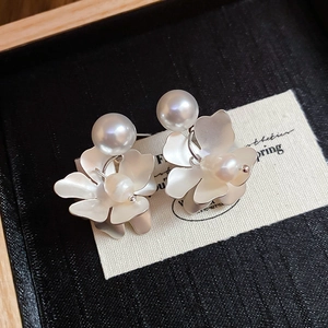 Detail of matte white flower earrings with pearls resting on a vintage wooden box