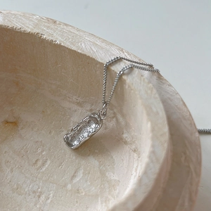 Macro detail of irregular oval silver pendant with textured surface on a ceramic bowl