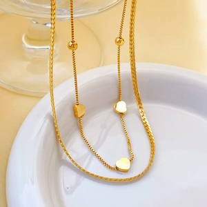Detailed macro view of a gold heart pendant and bead charms on a layered chain necklace