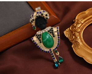 Detailed view of vintage exotic brooch with green crystals and pearl tassel accents