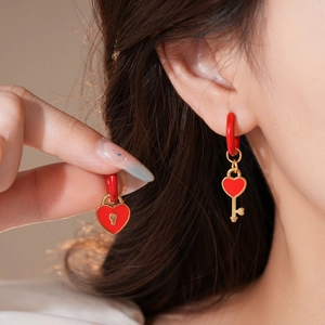 Detail view of asymmetric red heart lock and key earrings in gold stainless steel