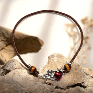 Macro view of woven bracelet featuring tiger eye beads and red strawberry pendant