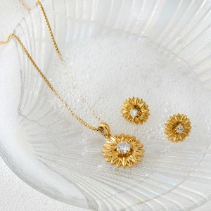 Goldenes Set aus Sonnenblumen-Halskette und Ohrringen mit Zirkonia auf Glasteller