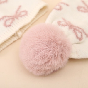 Macro detail of soft pink faux fur pompom and knitted bow pattern on baby winter hat
