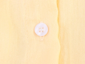 Détail des boutons blancs sur le tissu jaune pâle de la robe chemise en dentelle