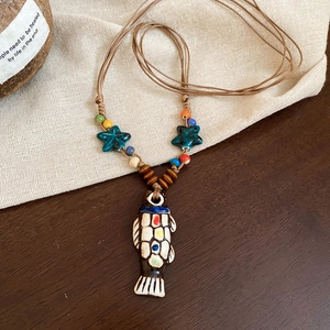 Detail of handcrafted ceramic fish pendant with starfish beads on a woven rope necklace