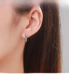 Détail de créoles en argent serties de zircones vertes marquises sur l'oreille du mannequin