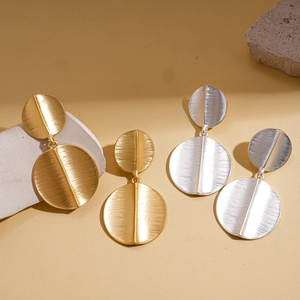 Brushed geometric metal disk drop earrings in gold and silver set on a stone display