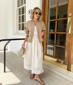 Outdoor street style view of khaki bomber jacket paired with white long skirt and beige clutch