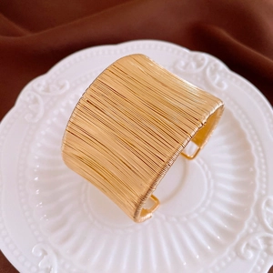 Détail d'un large bracelet manchette doré avec une finition texturée de fils métalliques