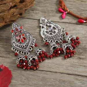 Detail of bohemian silver tassel earrings with red beads on a rustic wooden surface