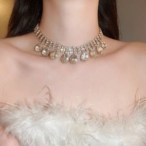 Close-up of gold choker necklace with teardrop rhinestones on a model in white feathers