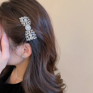 Detailed close-up of a silver bow hair clip with sparkling rhinestones and a central pearl