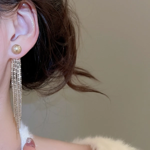 Close-up of golden tassel earrings with pearl stud on model in soft lighting