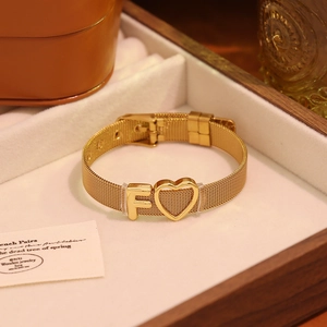 Détail d'un bracelet en maille dorée avec lettre F et breloque cœur dans un écrin