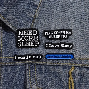 Detailaufnahme von fünf Emaille-Pins zum Thema Schlaf auf blauem Denim-Stoffhintergrund