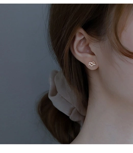 Close-up of heart-shaped gold stud earrings with cubic zirconia worn by a model