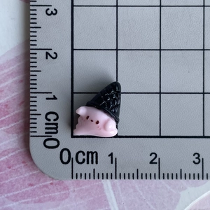 Detailed macro shot of a mini pink pig resin charm with black hat next to a ruler for size