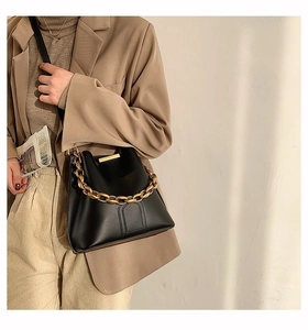 Detail of the high-quality black bucket bag featuring a thick gold chain strap and texture