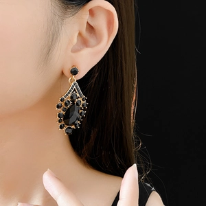 Close-up of gold pendant earrings with black gemstones worn by a model against black