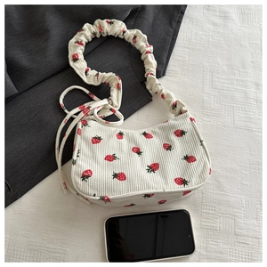 Flat lay of strawberry print corduroy shoulder bag with ruched strap and phone for scale