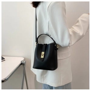 Fashionable black leather bucket bag with gold clasp shown on a model in a white blazer