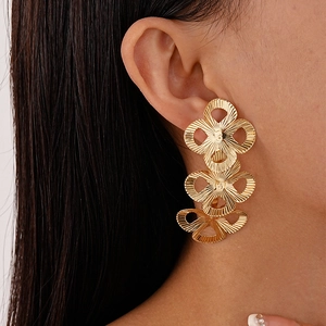 Close-up of triple gold clover drop earrings with striped metal texture on female model