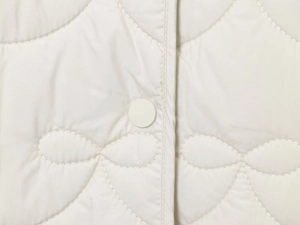 Detailed close-up of white quilted jacket featuring snap buttons and gourd stitching