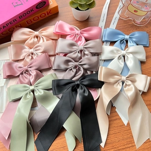 Various colored satin ribbon bow hair clips displayed on a wooden surface with lifestyle props