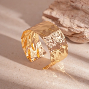 Modern wide gold open cuff bracelet with irregular wrinkled texture on stone base