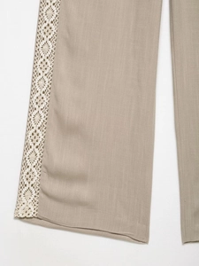 Detail shot of beige linen trousers featuring intricate white lace embroidery on the side