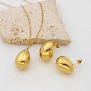Elegant gold teardrop necklace and earrings set displayed on a minimalist stone