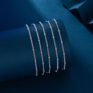 Macro detail of minimalist silver bead chain bracelets wrapped on a blue cylinder