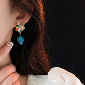 Detail of blue strawberry drop earring with rhinestones worn by a model on dark background