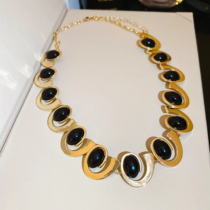 Close-up of gold geometric necklace featuring oval black stones and abstract metallic links