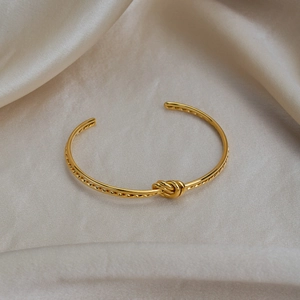 Vue détaillée d'un bracelet nœud doré sur soie soulignant la texture polie et l'élégance