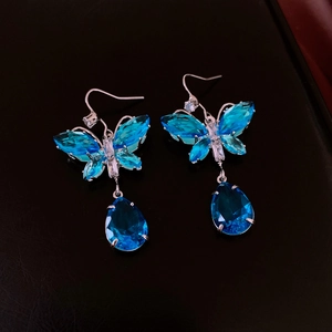 Nahaufnahme von Schmetterling-Ohrringen mit blauen Edelsteinen und silbernen Haken