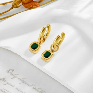 Elegant gold drop earrings with rectangular emerald gemstone on white textured tray