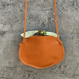 Detail of orange fruit-shaped crossbody bag with lychee texture and green leaf accent