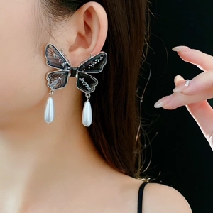 Close-up of butterfly earrings with transparent wings and teardrop pearls on model