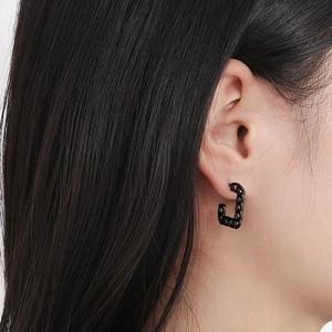 Close-up of matte black Cuban chain earrings worn on ear showing geometric hollow design