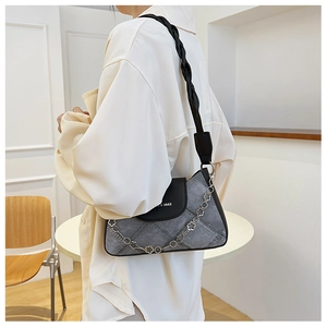 Detailed view of grey denim underarm bag with metal floral chain on model's shoulder
