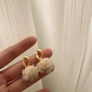 Detail of white plush earrings with matte gold hoops held by hand for scale