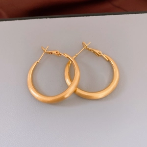 Dettaglio di grandi orecchini a cerchio placcati oro 18k con texture opaca spazzolata