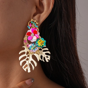 Macro shot of tropical earrings with colorful sequins and green monstera leaf pendant