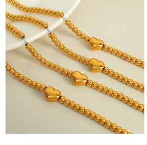 Détail du bracelet à perles plaqué or 18k avec pendentif coeur sur fond minimaliste