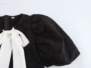 Detail der Puffärmel und weißen Schleife an einem schwarzen Jacquard-Kleid