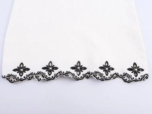 Detail of white dress hem with black wavy embroidery and faux pearl embellishments